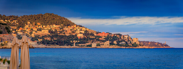 White umbrellas line a pebbled beach under golden sunset clouds in Nice, France