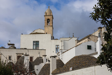 Fototapeta premium traditional trulli houses with conical stone roofs and white walls under a bell tower in alberobello, puglia, italy. authentic mediterranean village.