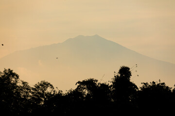 The silhouette of mountains and volcanoes at sunset, with a line of trees in the foreground, near the city of Malang, Java, Indonesia