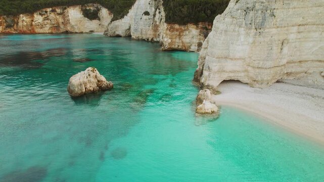 Tranquil turquoise cove with white cliffs and a lone figure of woman standing on a rock in Kefalonia serene summer scenery from above