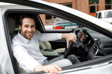 Obraz premium Test drive, buying and renting car, auto business and road to office. Happy european young attractive man in white shirt driving in city, checking transport, stops and opens door, free space