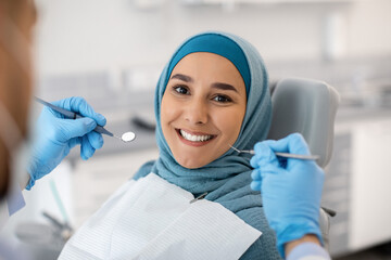 Portrait Of Happy Muslim Woman Sitting At Dentist Chair In Modern Clinic And Looking At Camera,...