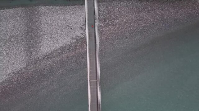 Top-down aerial drone view of a cyclist crossing a bridge from Switzerland into Liechtenstein, highlighting movement, infrastructure, and scenic surroundings.