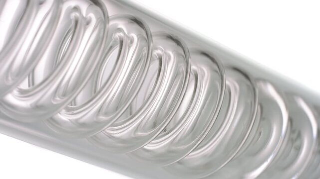 Macro shot of glassy transparent liquid flowing through the spiral of an inclined coil laboratory condenser, filling it up against white surface | Butylene glycol skincare cosmetic formulation idea