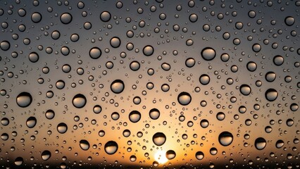 Close-up view of water droplets on a window pane with a blurred sunset in the background, creating a serene and reflective mood.