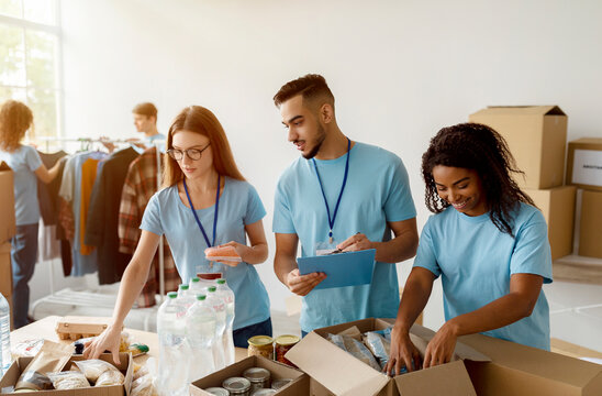 A young group of multiracial volunteers work together in a community charity donation center. They are sorting donated food into boxes to help support poor and homeless individuals in the local area.