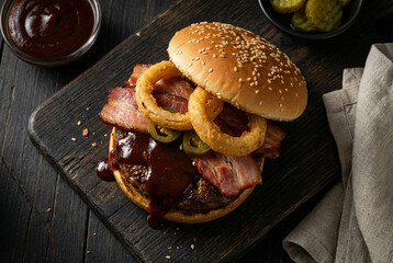 BBQ bacon burger with onion rings and jalapenos on wood
