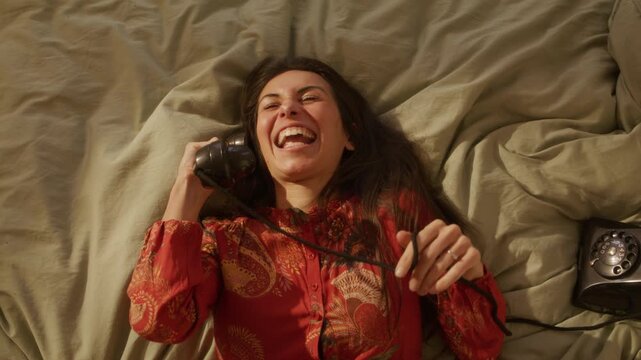 Stylish Dreamcore woman falls back talking on retro rotary phone while in bed