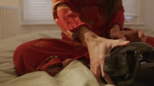 Retro dreamcore woman picks up and plops rotarty phone on bed and starts dialing - close up