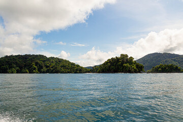 Tropical coastline with small forested islands and calm sea under blue sky and clouds