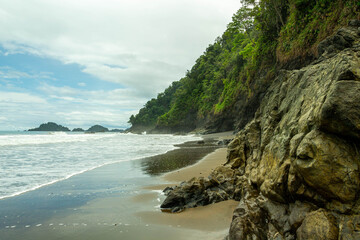 Rocky tropical beach with ocean waves and lush rainforest coastline
