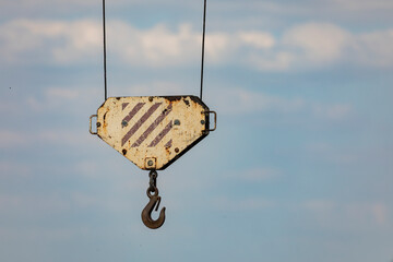 A somewhat rusty hook from a crane, hanging from metal cables, stands out against the blue sky.