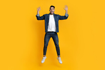 Cheerful handsome bearded young arab man jumping up in the air, raising hands up, copy space,...