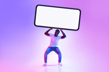 Handsome young black man poses with a large smartphone under vibrant neon lights. The blank screen...
