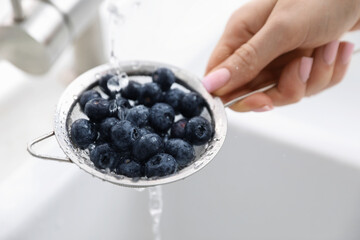 Woman washing blueberries in sieve at sink, closeup