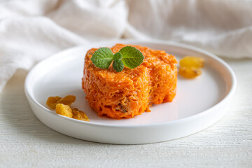 Carrot casserole with dried fruits in heart shape on white plate, side view, close up