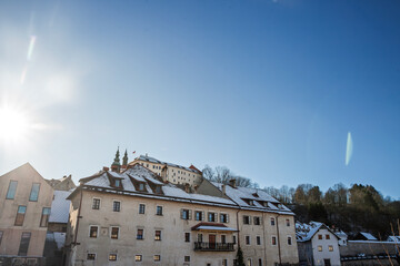 Panoramic winter view of Skofja Loka, Slovenia with snow-covered roofs and the medieval Loski Grad - Loka Castle on the hill. Clear blue sky and sunlight over the historic town center.