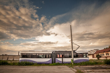 A purple and white tram of the Timisoara transport system parked on a track near the city outskirts. Tramvaiul in timisoara is the main public transportation system of the city.