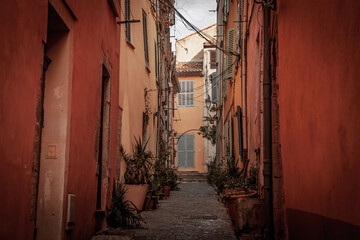 narrow street in Vieux Hyeres, French riviera, France, with pastel facades, shutters and potted plants, showing a typical Provencal village street paved with cobblestones.