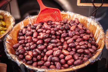 A large wooden bowl filled with fresh black olives at a market stall. A red scoop rests on top of the heap of shiny cured fruit ready for sale on a typical market of provence in france.