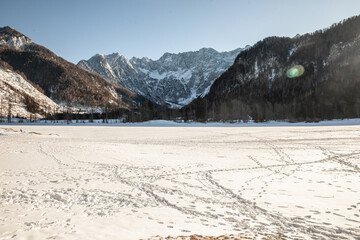 Snowy panorama of Zgornje Jezersko with Goli Vrh mountain rising beyond, showing rugged ridges, conifer forest, and winter light across the Julian Alps in northern Slovenia.