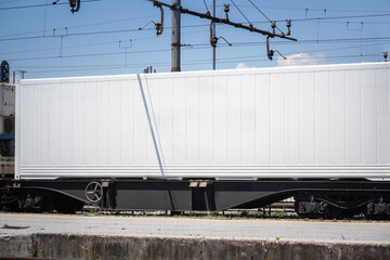 A white refrigerated shipping container loaded onto a railway wagon at a train station platform, a symbol of logistics and intermodal transportation and cold chain.