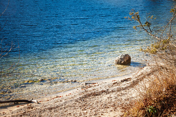Crystal clear shallow water at Lake Bohinj reveals pebbles and lakebed stones along the shore, highlighting clean freshwater, strong transparency, calm ripples environmental quality in an alpine lake.