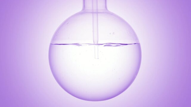 Close shot of crystal clear liquid injected through a long dropper into a round-bottom flask, causing swirls and bubbles on purple ramp background