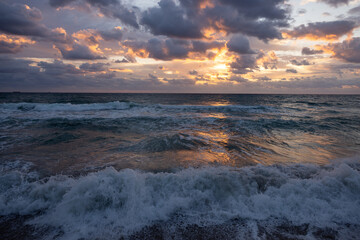 Dramatic sunrise over ocean waves with storm clouds and golden reflections