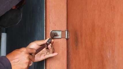 A thief uses a knife to break a padlock while attempting to rob a house.