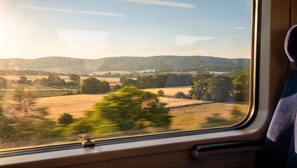 Scenery of rolling hills and trees seen from a train window on a sunny day. Travel, journey, and transportation concept. Beautiful landscape.