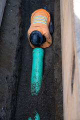 Construction worker in deep trench protected by Trench Box, coffin, while installing new 8 inch sewer line pipe under the road, building out infrastructure for new housing development
