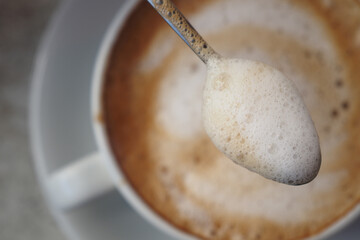 Cup of coffee with foam and spoon over a table