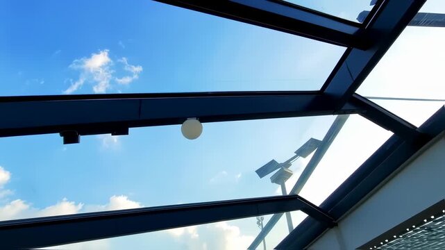 Glass ceiling with steel frame construction with blue sky view and white clouds
