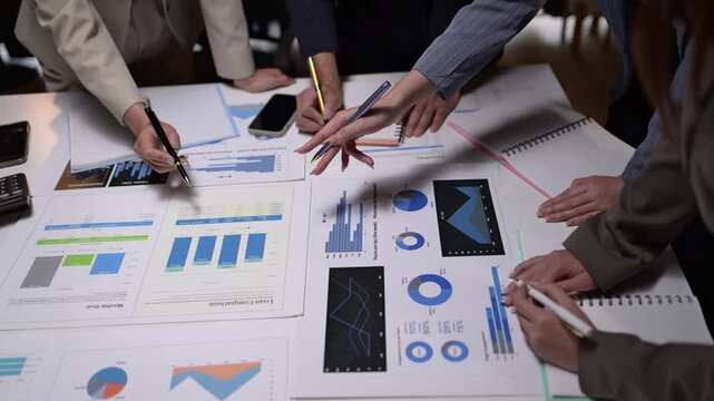 A group of people are working on a project and writing on a table. There are several papers with graphs and numbers on them