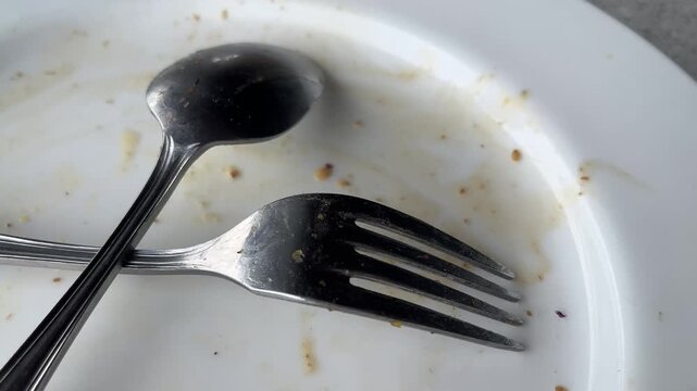 Empty white plate with leftover food and utensils after a meal. Top view, high angle, above, flat lay. close up. fork and spoon. stainless steel. crossed,