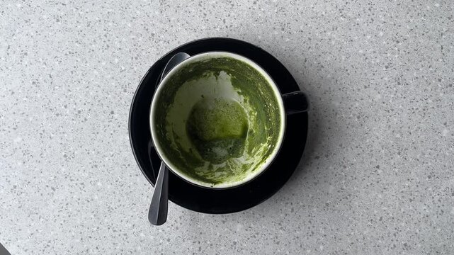 empty hot matcha latte cup after drinking. Black cup or mug with spoon. Glass table. Cafe, coffe shop. close up view. leftover. top view, high angle, above, flat lay. granite table. isolated.
