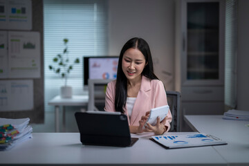 Asian businesswoman using calculator and digital tablet working on financial data in office at night