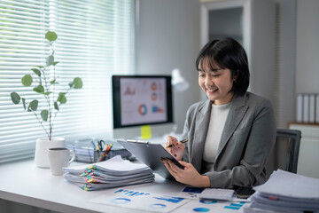 Asian businesswoman working with financial documents and using computer at office desk