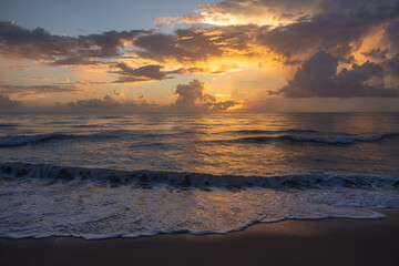Fototapeta premium Golden Sunrise Over Ocean Waves With Dramatic Clouds