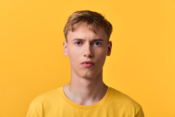 Fototapeta premium Yellow background with a male in a matching shirt, closeup on facial features and neutral expression, studio lighting enhances color contrast for a bold modern fashion mood