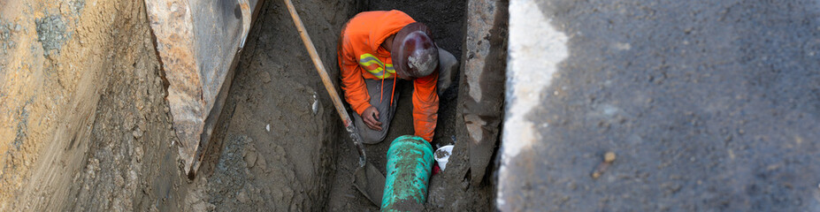 Construction worker in deep trench protected by Trench Box, coffin, while installing new 8 inch...