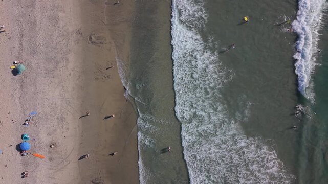 Moonlight beach in Encinitas, California. People enjoy a day at the beach. Top down drone view, ascending.