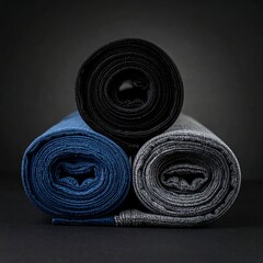 Three fabric rolls, one black, one blue, and one grey, stacked and lit against a dark backdrop. The cylinders' textures are visible