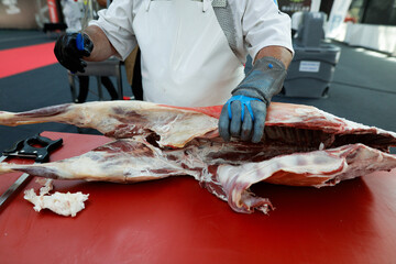 Details with the hands of a butcher, a knife in one and a metal glove in the other, cutting a pork carcass