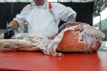 Details with the hands of a butcher, a knife in one and a metal glove in the other, cutting a pork carcass