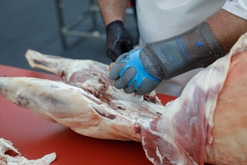 Details with the hands of a butcher, a knife in one and a metal glove in the other, cutting a pork carcass