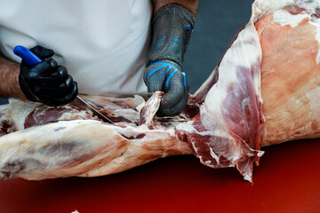 Details with the hands of a butcher, a knife in one and a metal glove in the other, cutting a pork carcass