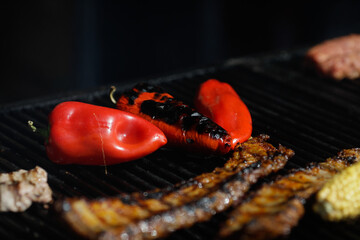 Corn, red paprika and pork ribs on an outside charcoal metal grill