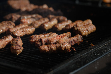 Romanian traditional mici (mititei or rolled minced meat) on an outside charcoal metal grill.